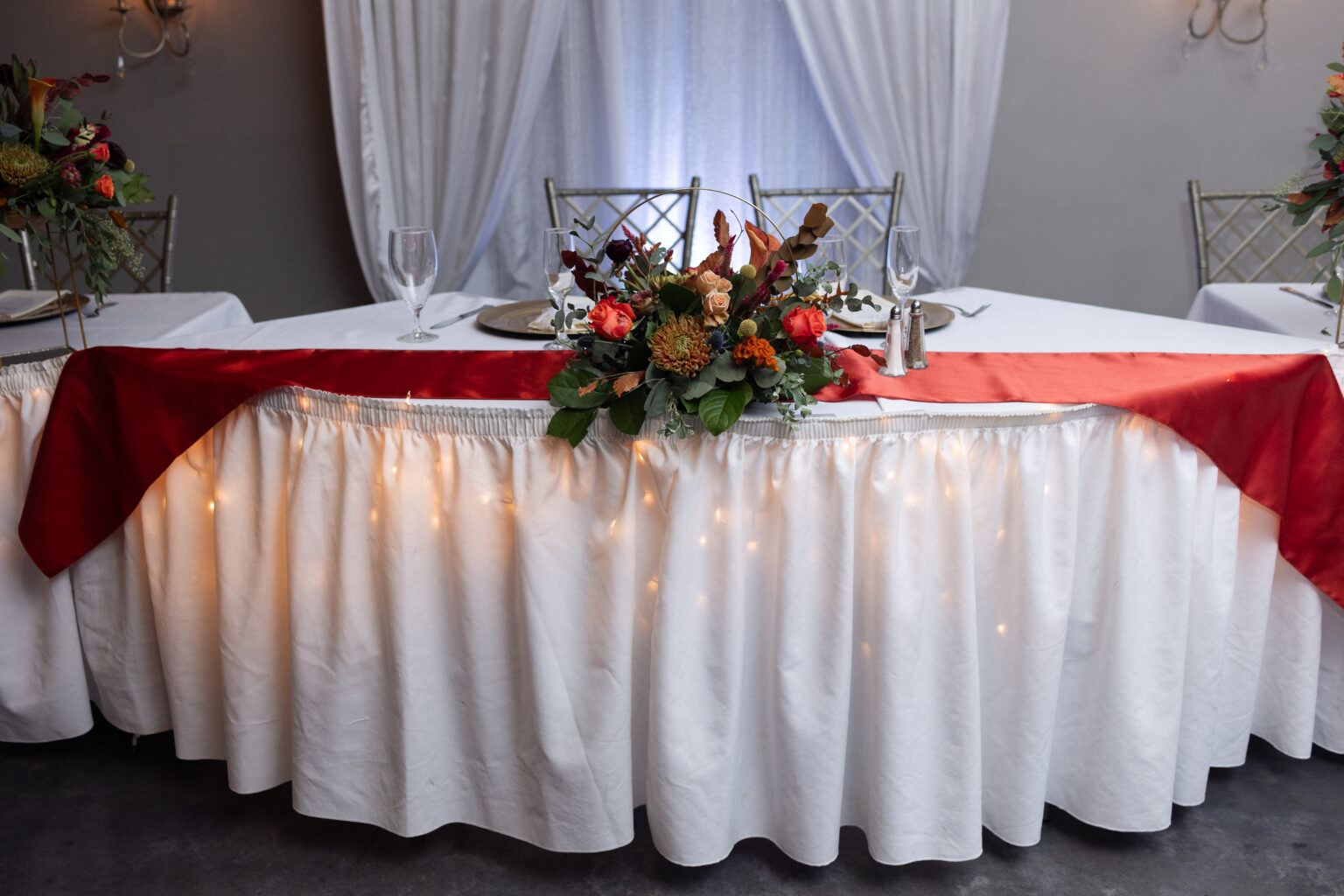 Sweetheart table with a burgundy runner and twinkle lights